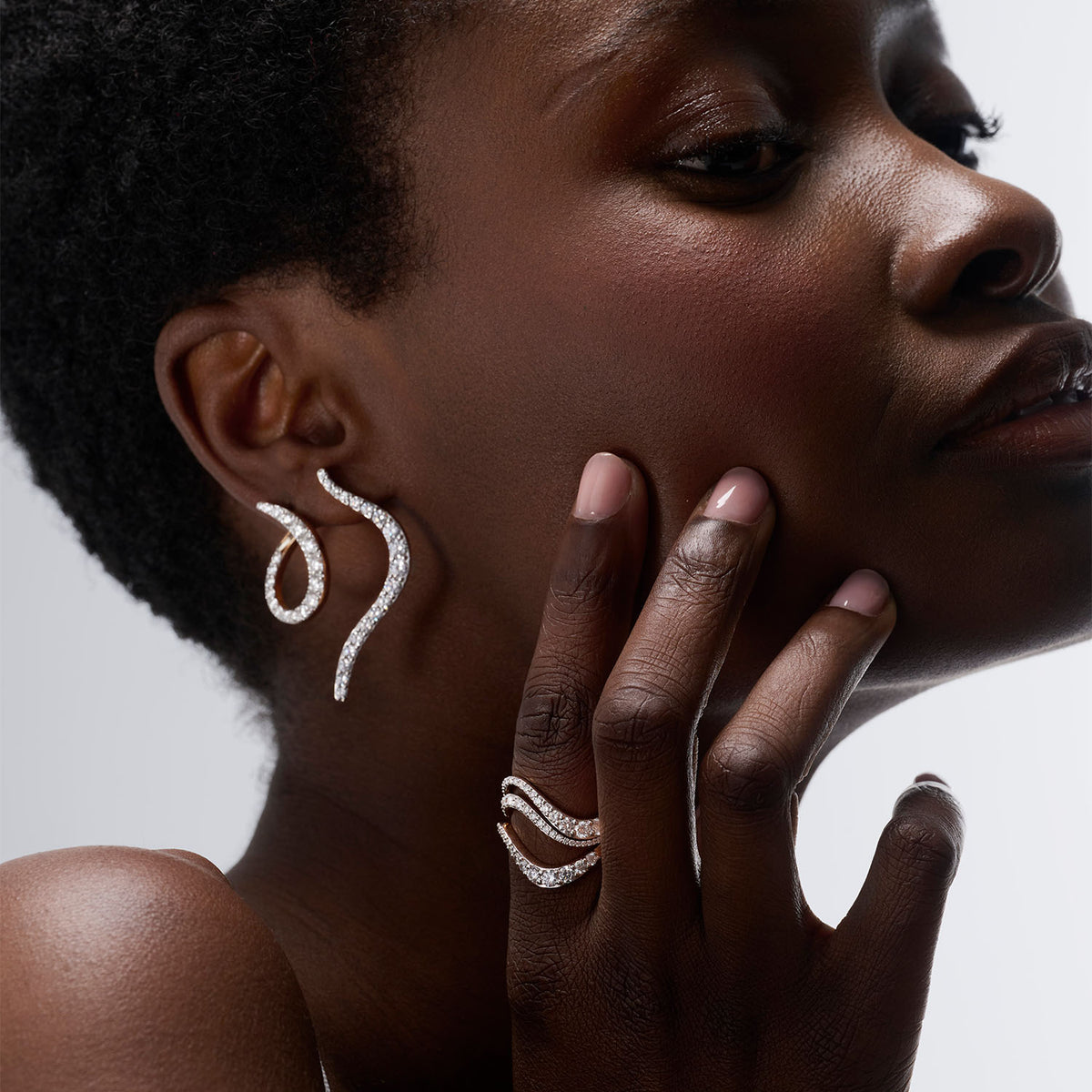 a young woman wearing an ear set composed of two pieces : a transformable brooch-earring and an earring. She also wear three ring inspired by the caustics, the luminous phenomen when light meet water. All pieces are crafted in 18k gold and set with natural diamonds in a gradient size.