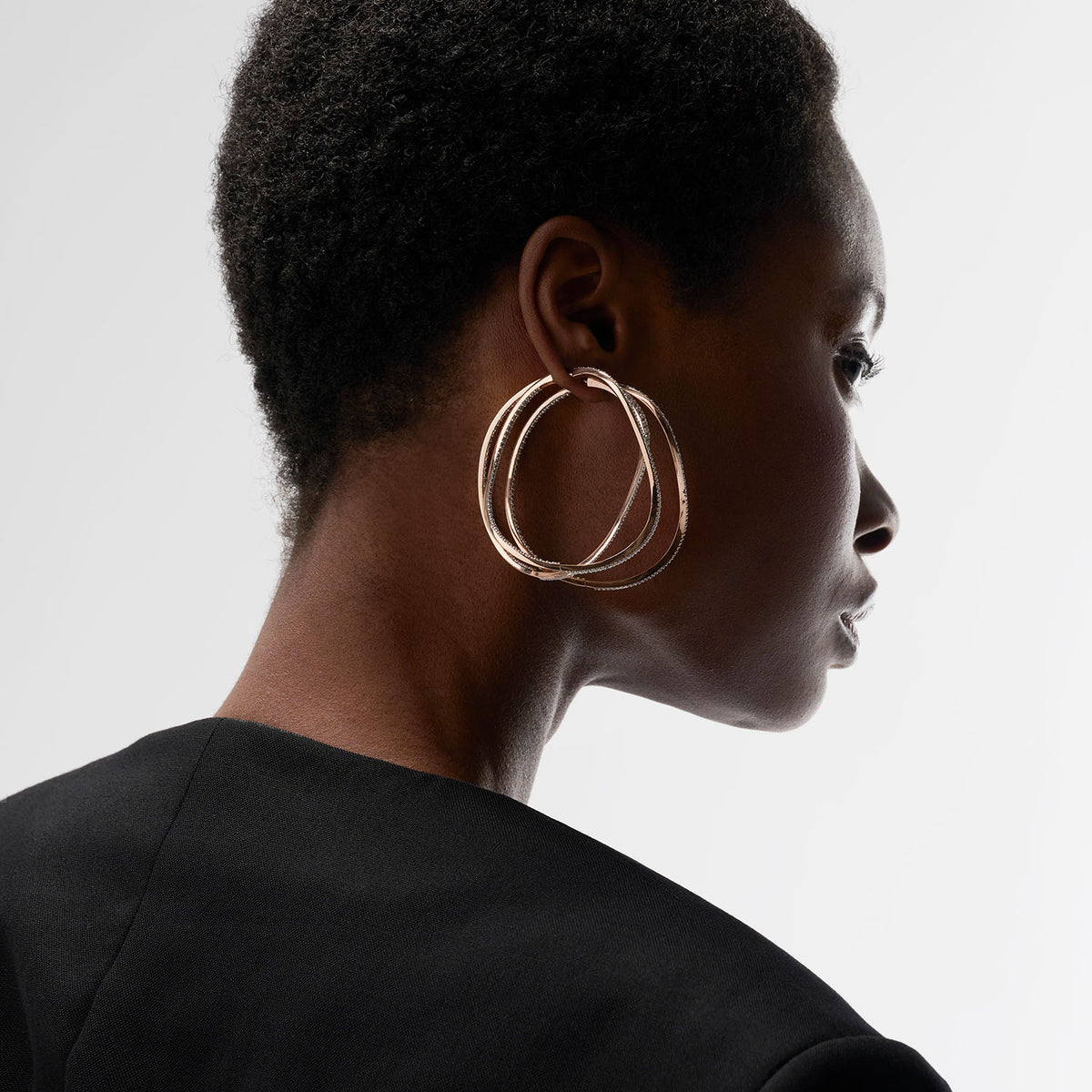 A young woman is wearing three transformable jewels : three bangle-hoop earrings. The fine jewelry pieces are crafted in 18k gold and set with natural diamonds. The set represent the caustic light which is the inspiration of the collection, blending the MARIE MAS two main sources of inspiration: water and light.