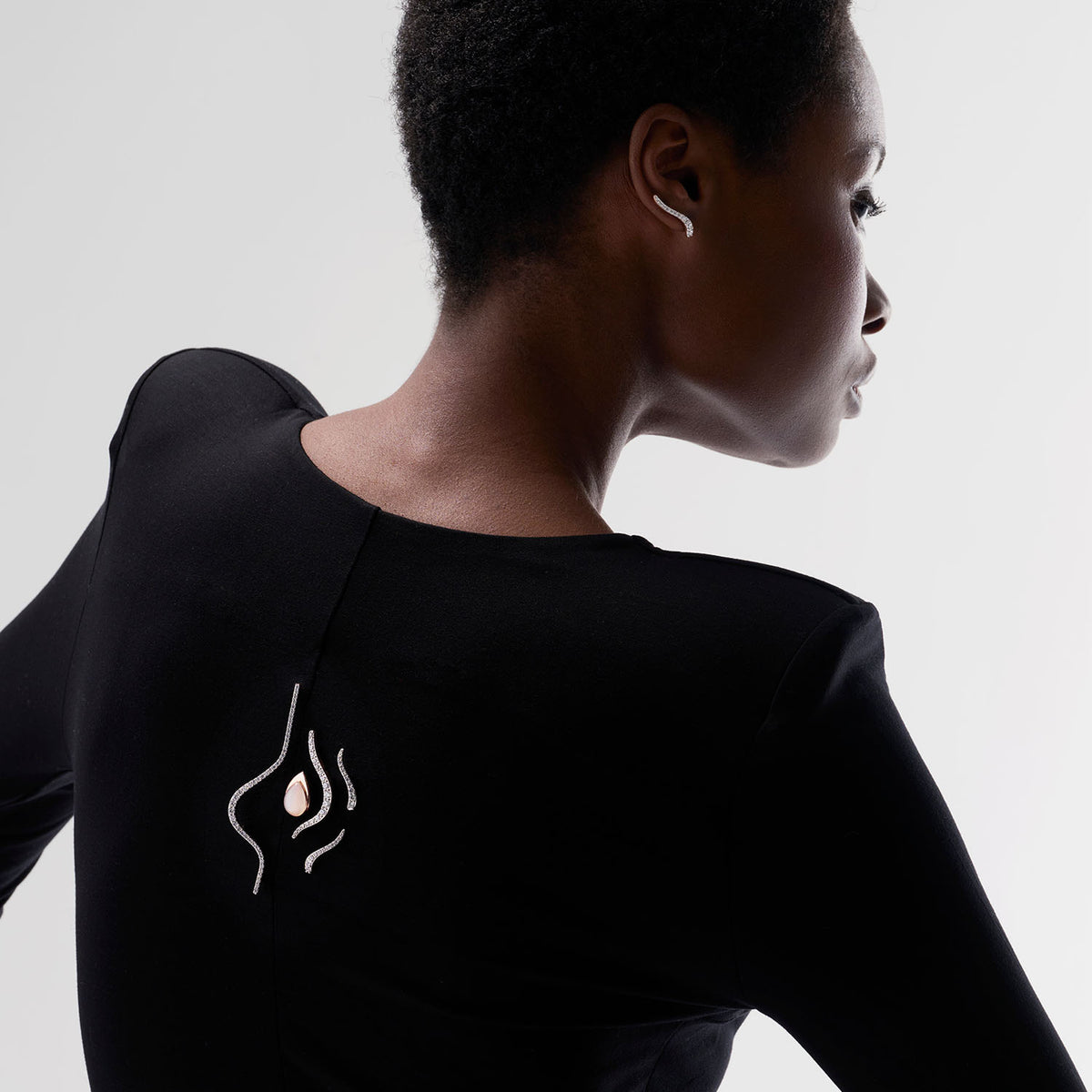 A young woman wearing a set of transformable brooch-earrings as brooches. It is composed of five pieces : each can be worn as brooch or as earrings. Crafted in 18k rose gold, they are set with natural diamonds or pear white moonstone. They can be worn together or separatly.