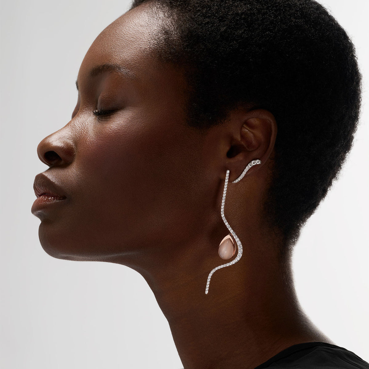 A young woman wearing set of three transformable jewels, brooch-earrings pieces. Crafted in 18k gold, they are set with natural diamonds or white moonstone. The white moonstone piece can be attached to the long earring thanks to an ingenious system.