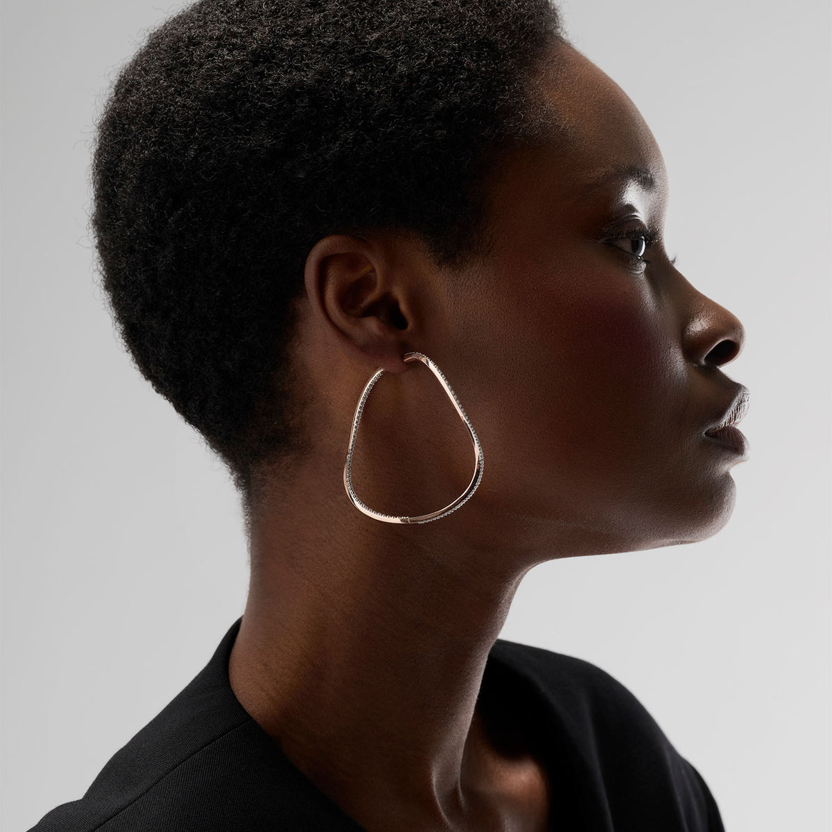 A young woman wearing a transformable jewel : a bangle-hoop earring presented as an earring here. This piece is crafted in 18k rose gold and set with natural diamonds. Thanks to an ingenious patented mechanism, the jewel switch from a bangle to an earring.