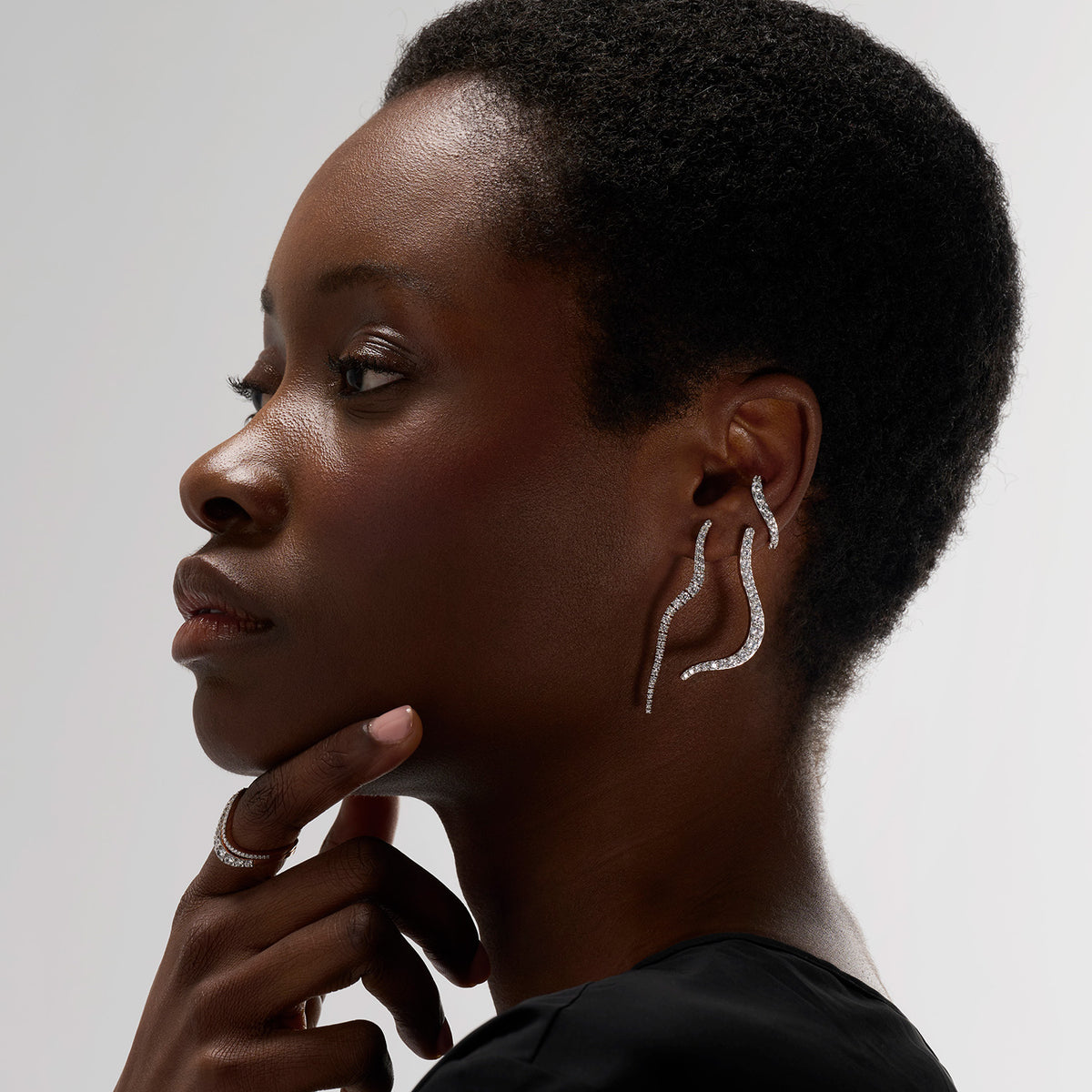 A young woman wearing a set of three pieces featuring an earring, a transformable brooch-earring jewel, and an ear jewel designed to be worn on non-pierced ears as well. This set brings light and creates luminous lines along the ear.