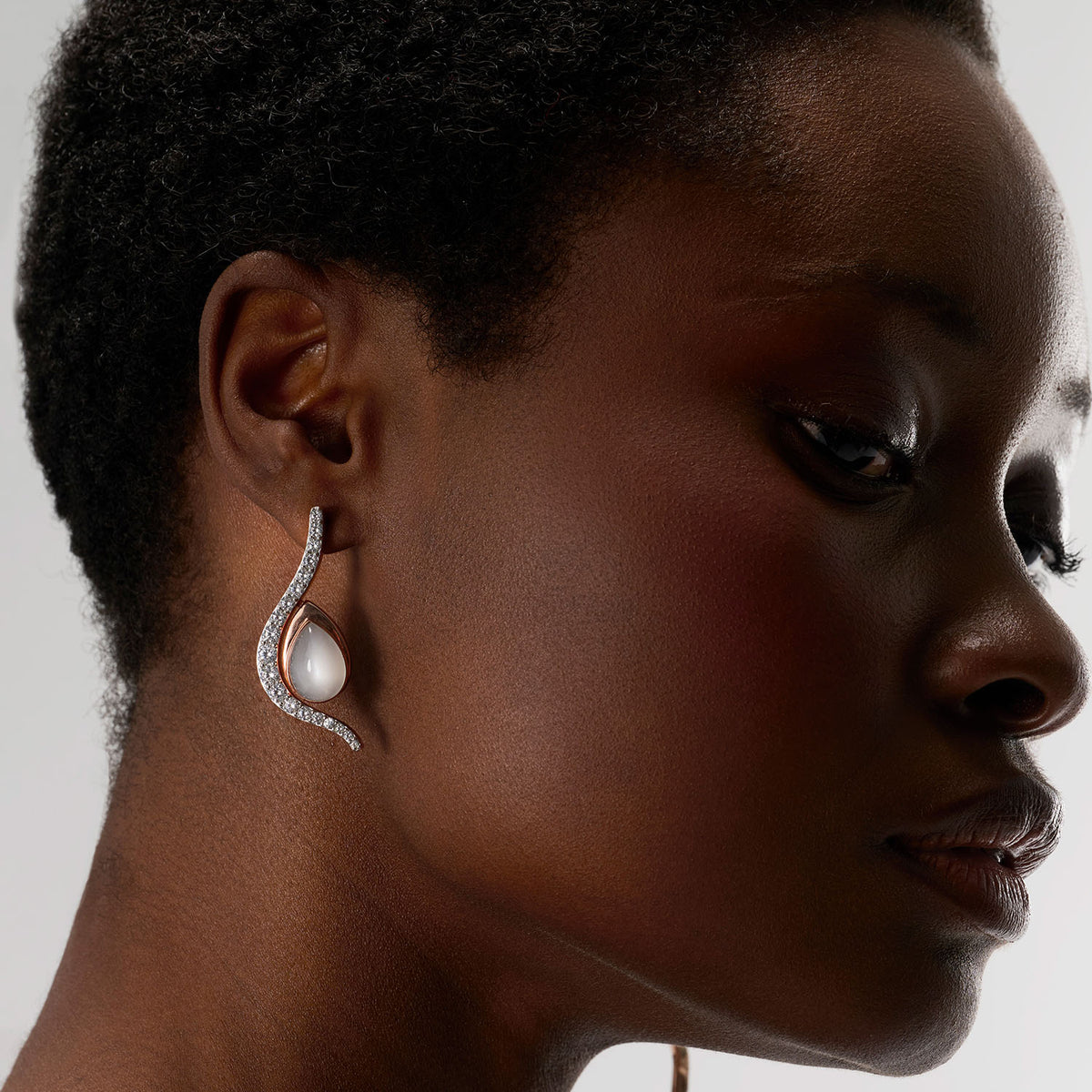 An earring composed of two different pieces, two brooch-earrings : one is an undulating diamonds line and a drop set with a pear-shape white moonstone. The pieces can be worn attached to or detached, individually. The pieces are crafted in 18k rose gold.