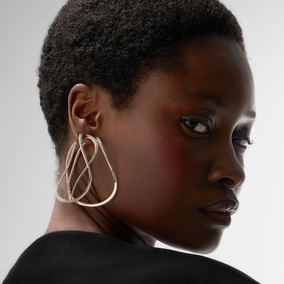 A young woman is wearing three transformable jewels : three bangle-hoop earrings. The fine jewelry pieces are crafted in 18k gold and set with natural diamonds.