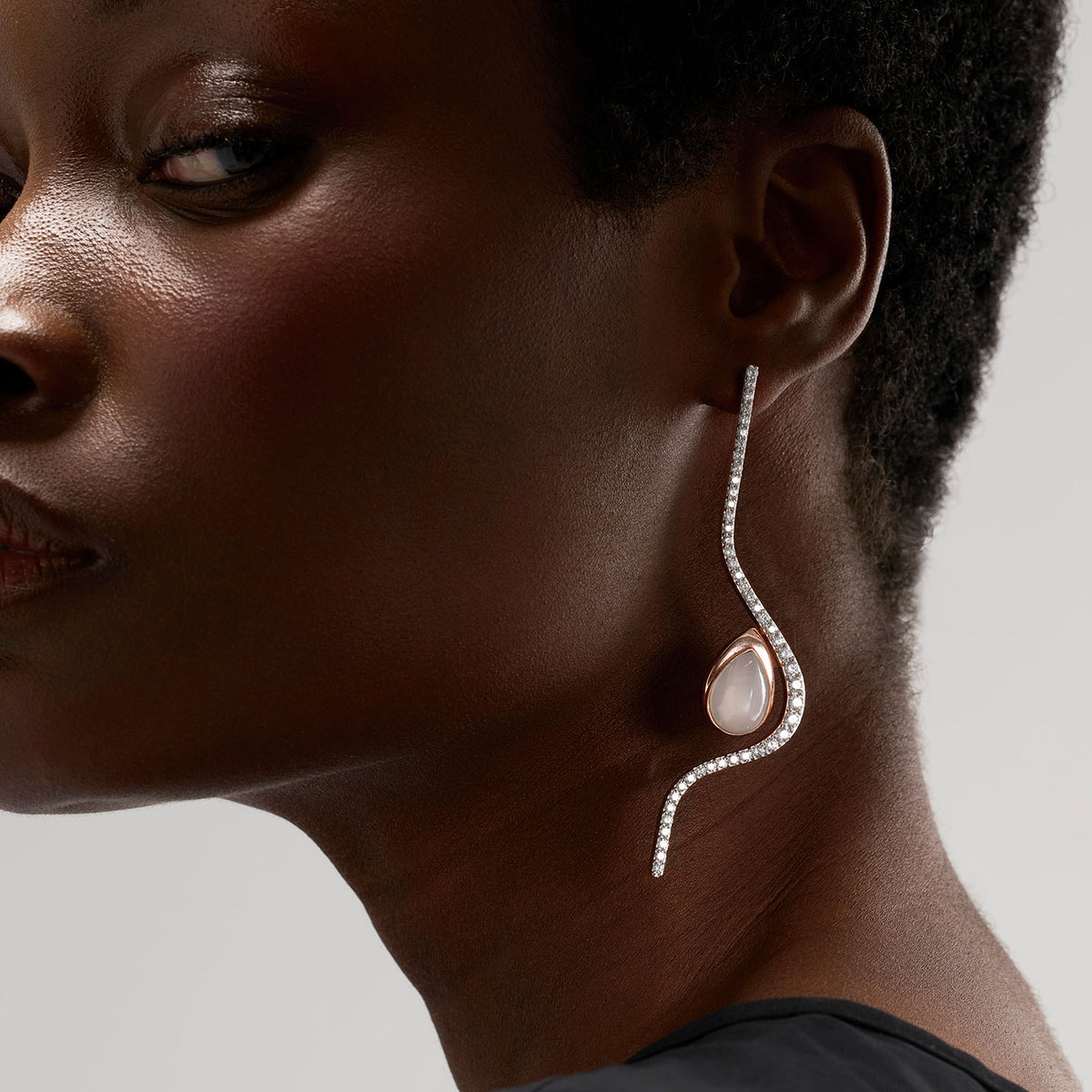 An earring composed of two different pieces, two brooch-earrings : one is a long undulating diamonds line and a drop set with a pear-shape white moonstone. The pieces can be worn attached to or detached, individually. The pieces are crafted in 18k rose gold.