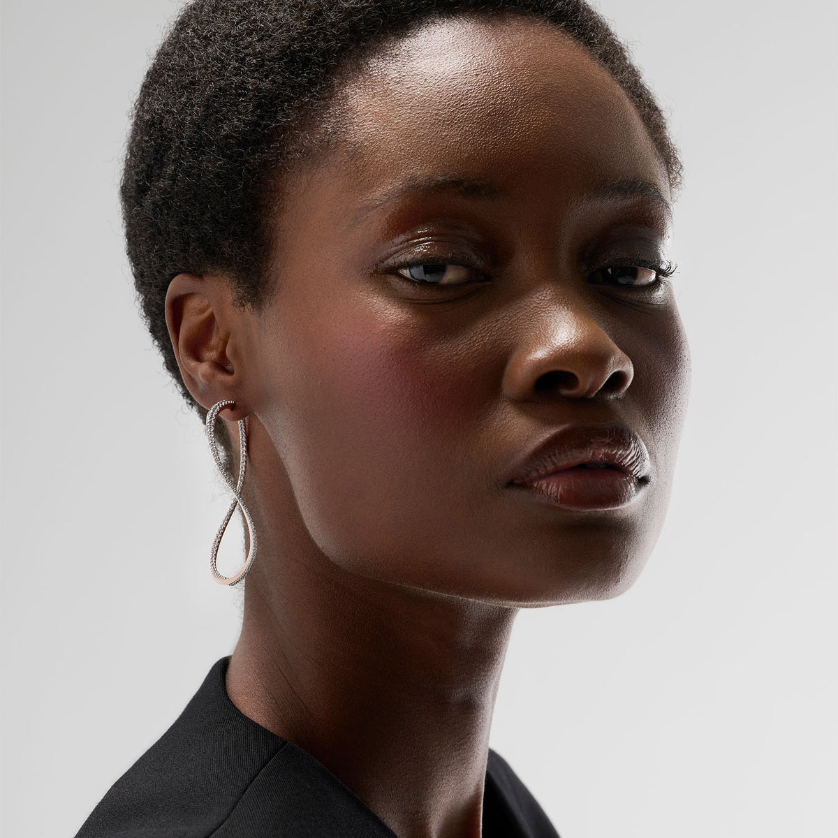 A young woman wearing a transformable jewel : a bangle-hoop earring presented as an earring here. This piece is crafted in 18k rose gold and set with natural diamonds. Thanks to an ingenious patented mechanism, the jewel switch from a bangle to an earring.