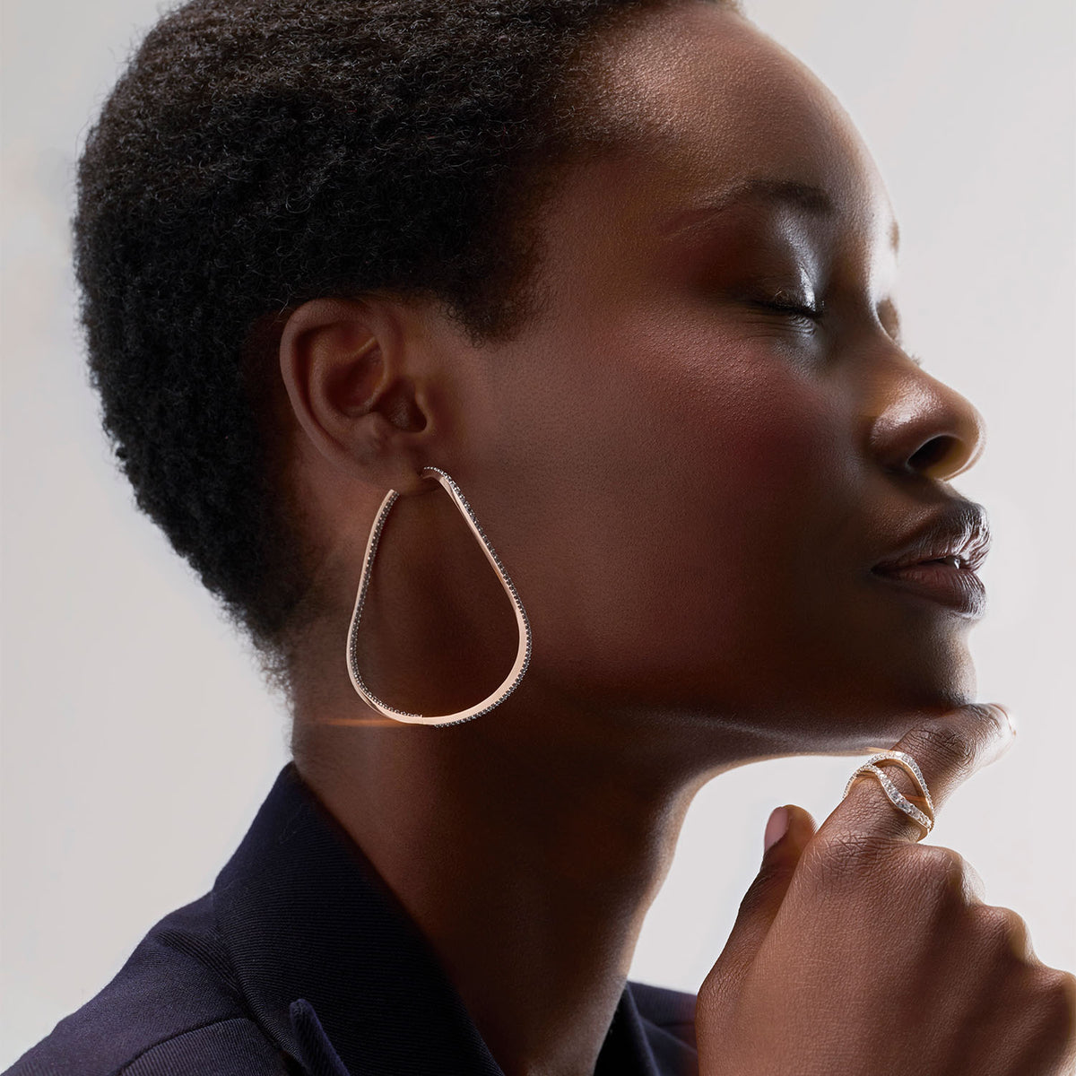 A young woman wearing a transformable jewel : a bangle-hoop earring presented as an earring here. This piece is crafted in 18k rose gold and set with natural diamonds. Thanks to an ingenious patented mechanism, the jewel switch from a bangle to an earring.