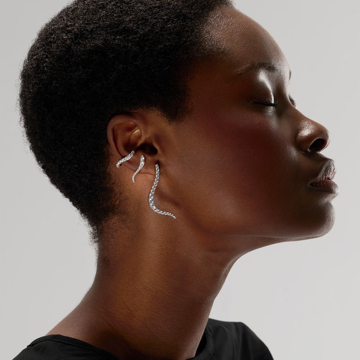 A young woman wearing an ear stack composed of three pieces : two transformable jewels from earrings to brooches, and an ear jewel that can be worn on unpierced ear. The pieces are crafted in 18k rose gold and set with natural diamonds.
