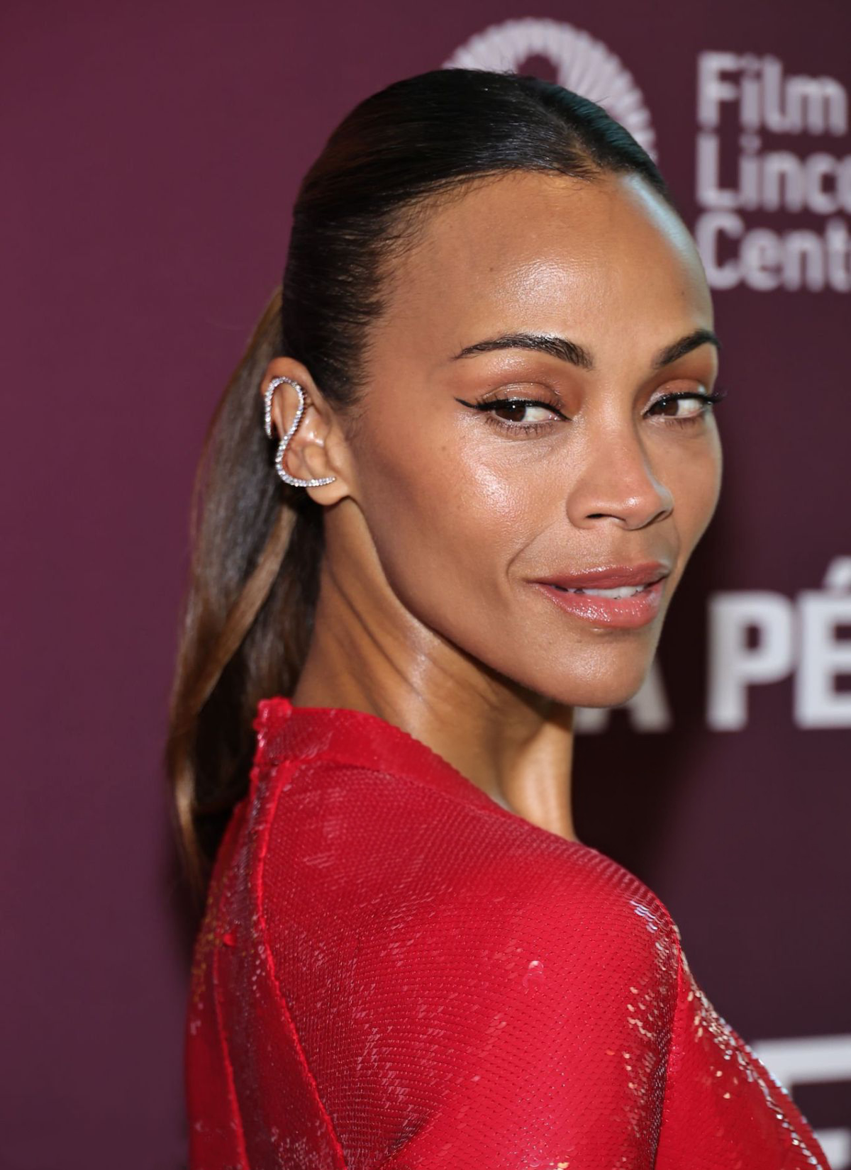 Zoe Saldaña poses at the New York Film Festival in a red embellished gown, showcasing a sculptural silver ear cuff that traces the outer curve of her ear.